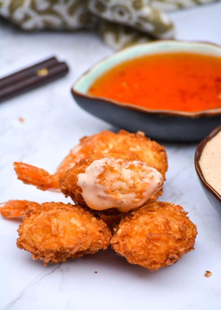 crispy coconut shrimp with a bite taken out of it resting on a pile of other coconut shrimp