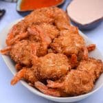 crispy air fryer coconut shrimp on a cream platter with dipping sauces in the background