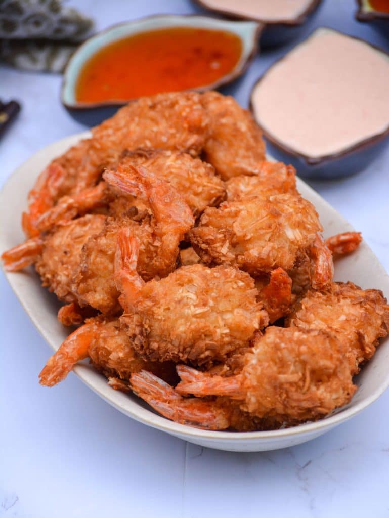 crispy air fryer coconut shrimp on a cream platter with dipping sauces in the background