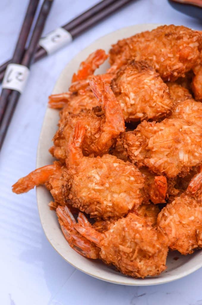 crispy air fryer coconut shrimp on a cream platter with dipping sauces in the background