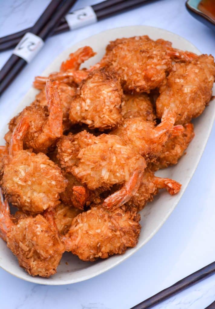 crispy air fryer coconut shrimp on a cream platter with dipping sauces in the background