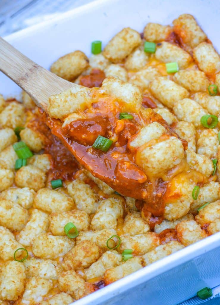 a wooden serving spoon in a chili cheese dog tater tot casserole