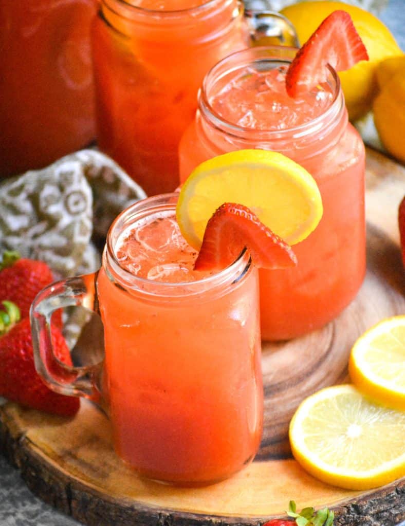 ice filled glasses of strawberry lemonade garnished with fresh lemon & strawberry slices