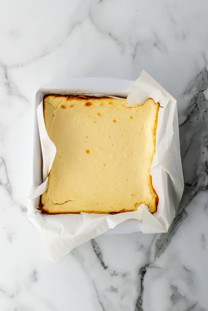 a square baked cheesecake in a parchment paper lined baking dish