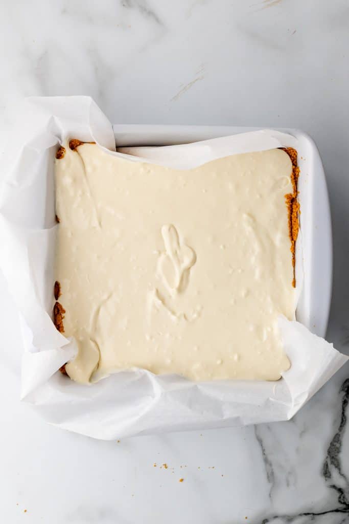 cheesecake filling shown on a graham cracker crust in a parchment paper lined baking dish
