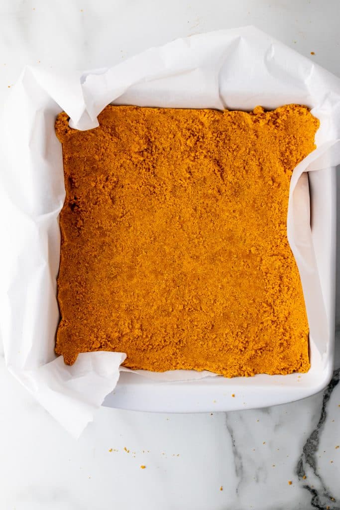 graham cracker crust in a parchment paper lined square baking dish