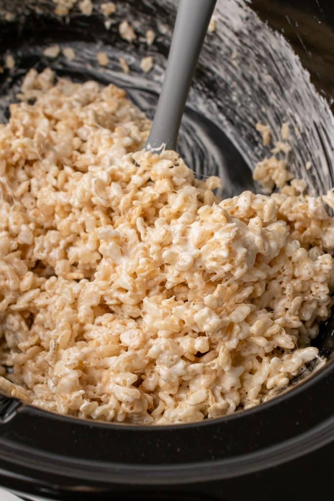 slow cooker rice krispie treats cereal and marshmallow mixture in a black crock