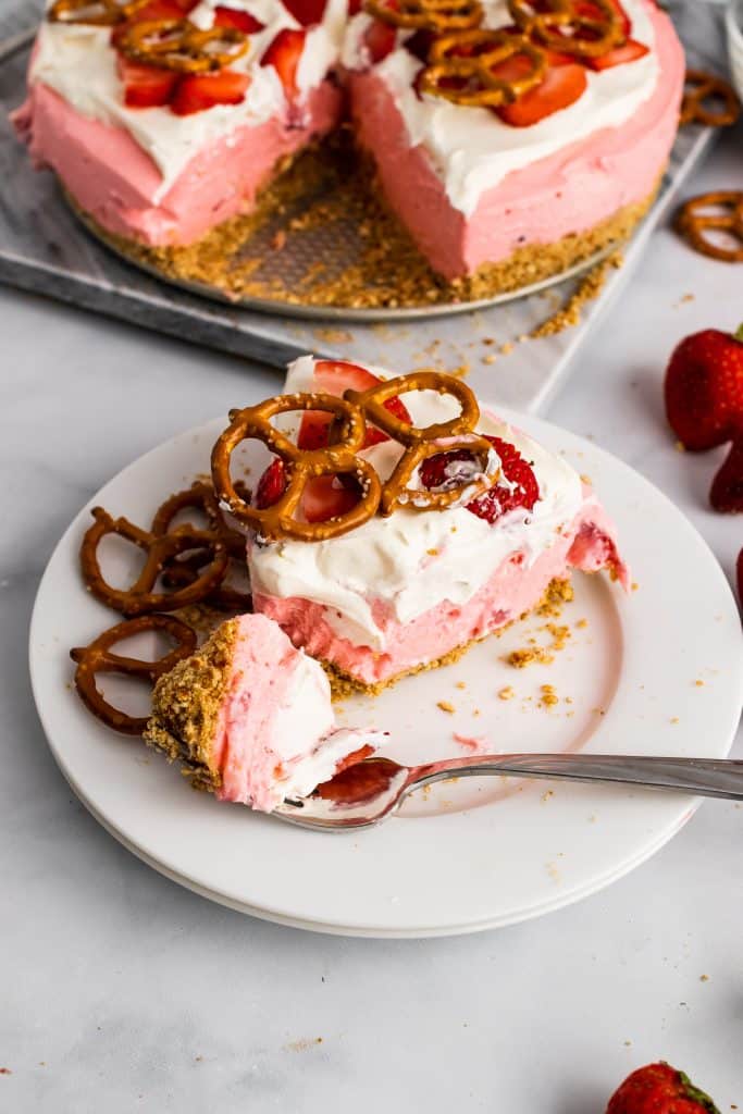 a fork digging into a slicer of strawberry pretzel pie on a white dessert plate