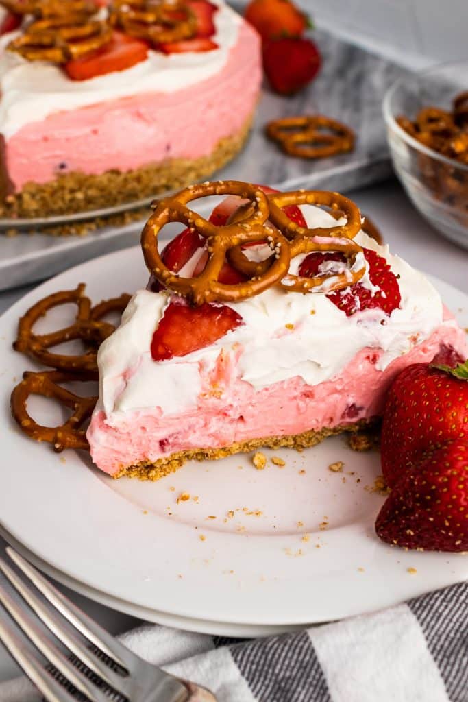 a slice of strawberry pretzel pie on a white plate with pretzels and fresh berries on the side