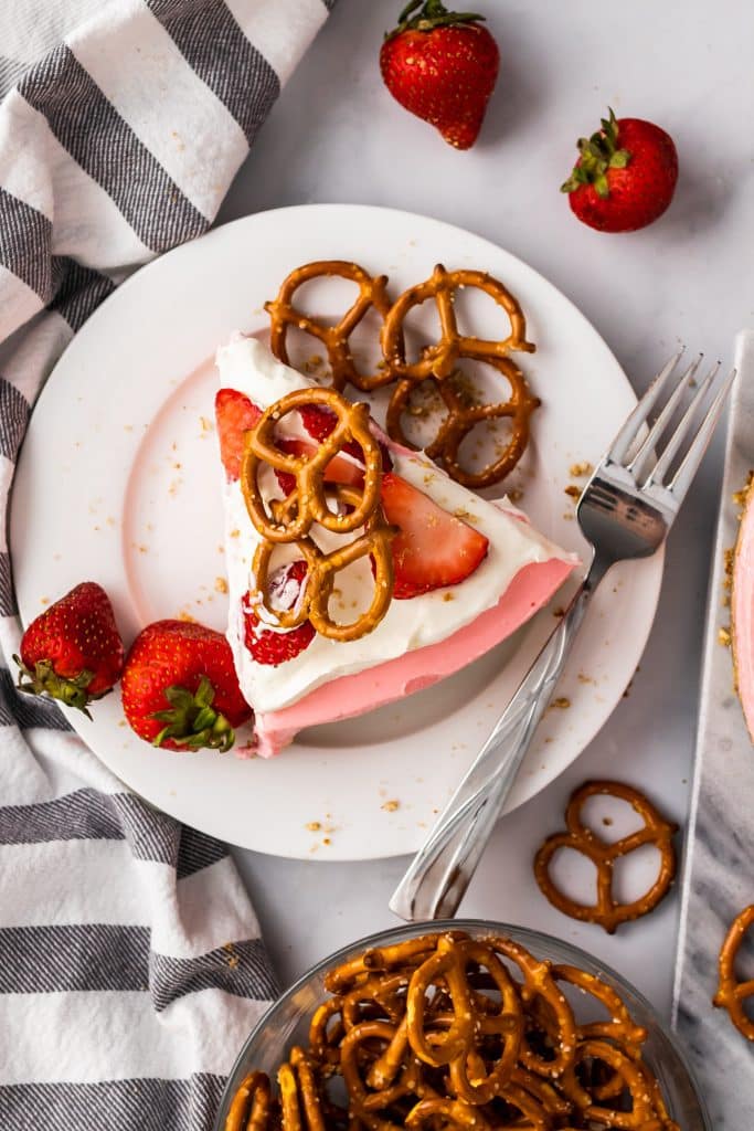 a slice of strawberry pretzel pie on a white plate with pretzels and fresh berries on the side