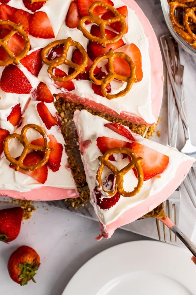 a piece of strawberry pretzel pie being removed from the whole on a silver serving spatula