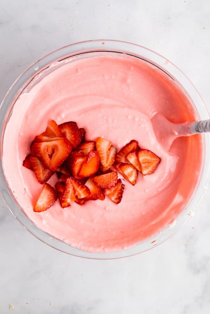 fresh sliced strawberries added to a mixing bowl filled with strawberry pie filling