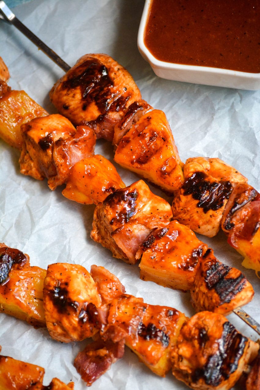 barbecue chicken kabobs with pineapple on metal skewers resting on white parchment paper