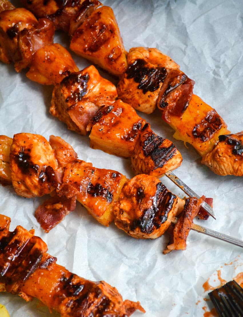 barbecue chicken kabobs with pineapple on metal skewers resting on white parchment paper