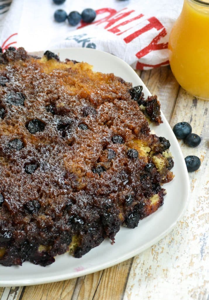 an upside down blueberry cake on a white platter surrounded by fresh blueberries