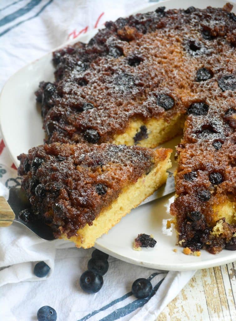 blueberry upside down skillet cake on a white platter with a slice being removed