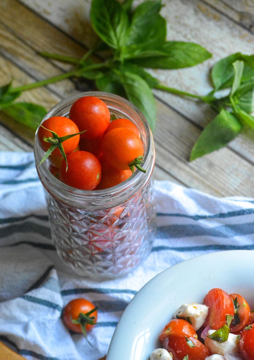 sweet cherry tomatoes stacked in a glass mason jar next to fresh basil leaves