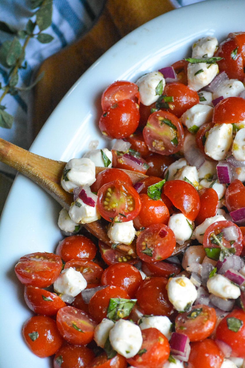 a wooden spoon in a white bowl filled with cherry tomato salad