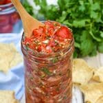 a wooden spoon stuck in a jar of cherry tomato salsa