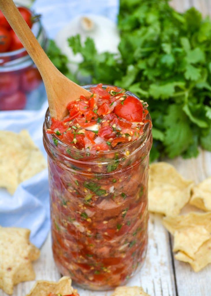 a wooden spoon stuck in a jar of cherry tomato salsa