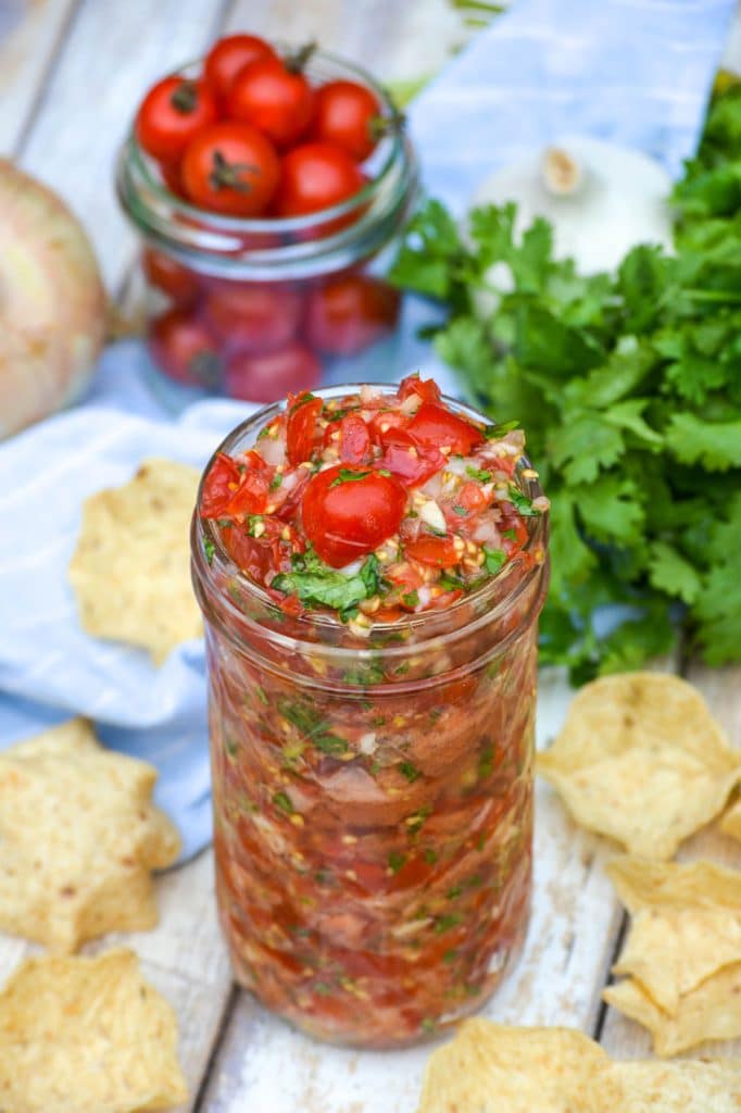 fresh cherry tomato salsa in a glass mason jar surrounded by tortilla chips
