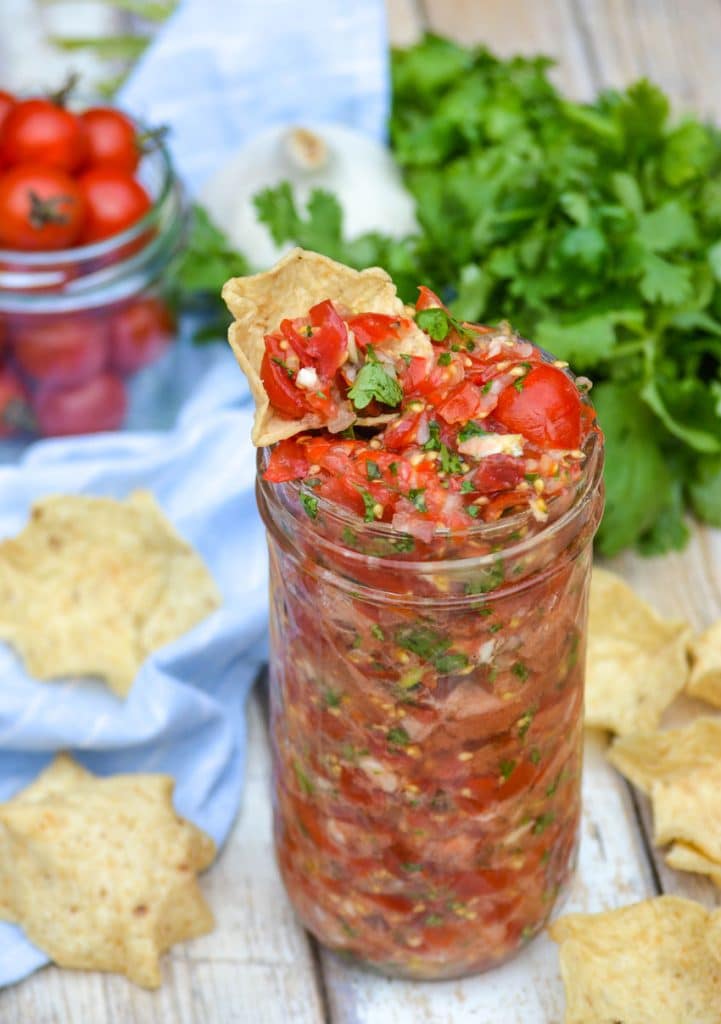 a tortilla chip dipped in a glass jar of sweet cherry tomato salsa