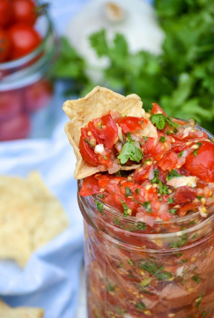 a tortilla chip dipped in a glass jar of sweet cherry tomato salsa