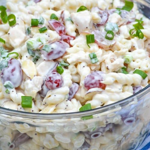 creamy poppy seed pasta chicken salad with grapes in a large glass mixing bowl with a wooden spoon on the side