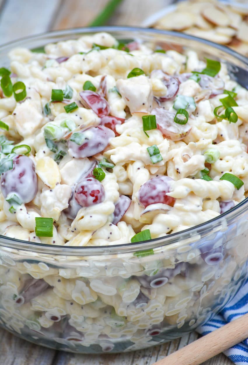 creamy poppy seed pasta chicken salad with grapes in a large glass mixing bowl with a wooden spoon on the side