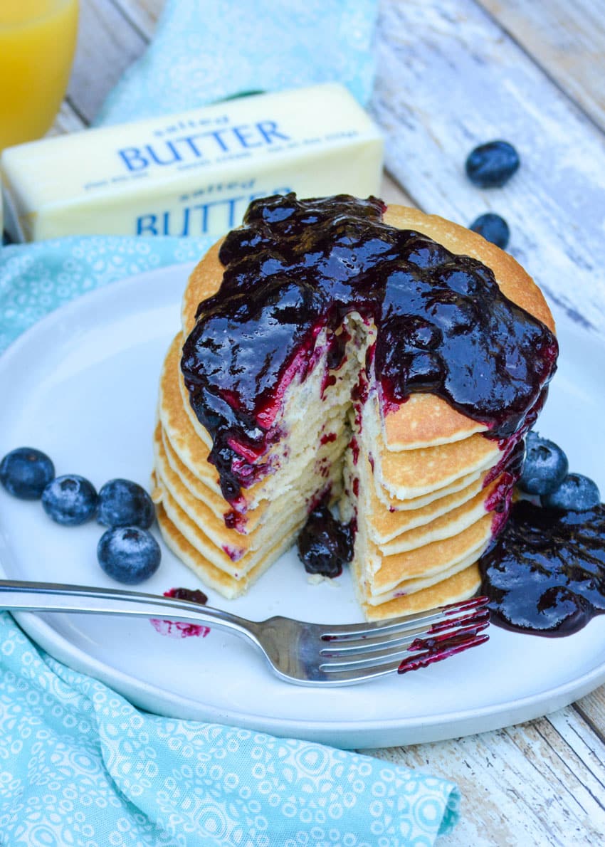 easy blueberry syrup recipe poured over a stack of pancakes