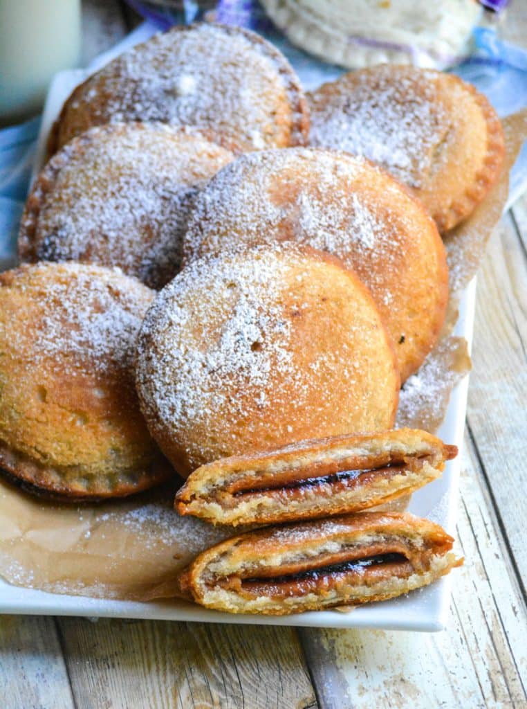 powdered sugar sprinkled fried uncrustables on a parchment paper lined white platter