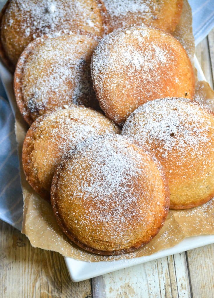 powdered sugar sprinkled fried uncrustables on a parchment paper lined white platter