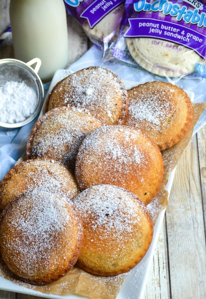 powdered sugar sprinkled fried uncrustables on a parchment paper lined white platter