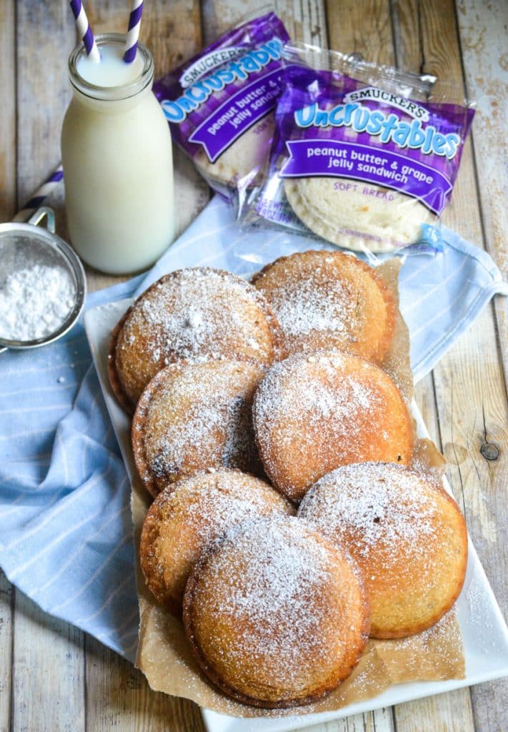 powdered sugar sprinkled fried uncrustables on a parchment paper lined white platter