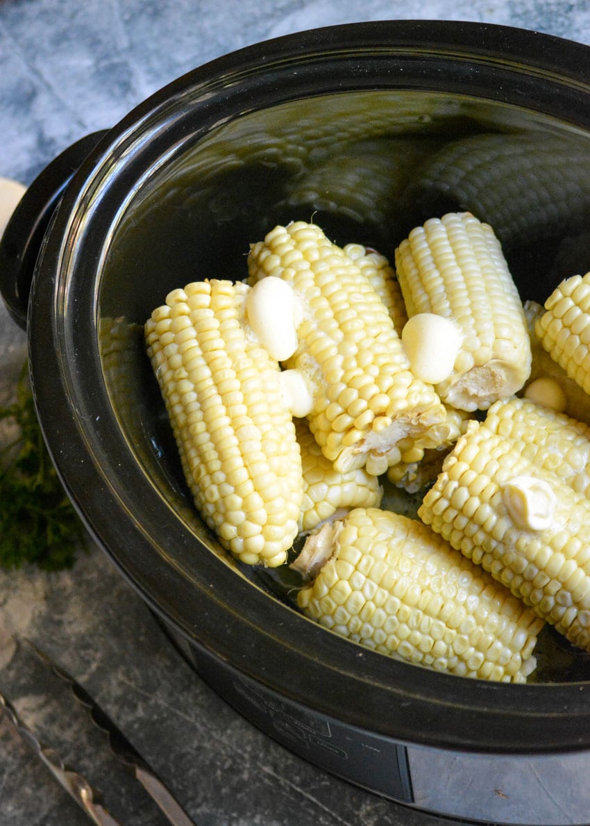 slow cooker corn on the cob topped with dollops of butter in a black crockpot