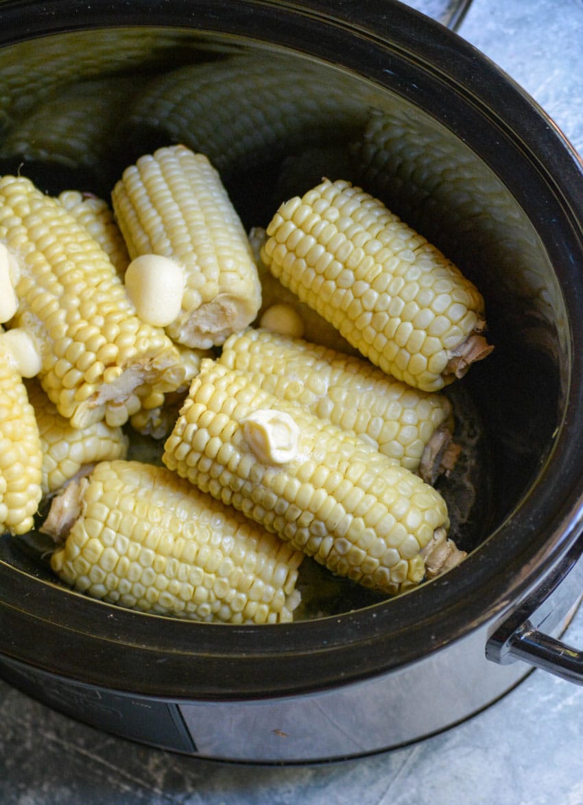 slow cooker corn on the cob topped with dollops of butter in a black crockpot