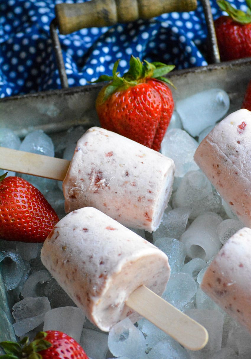 frozen strawberry cobbler pops on a bed of ice in a silver tray with fresh strawberries on the side