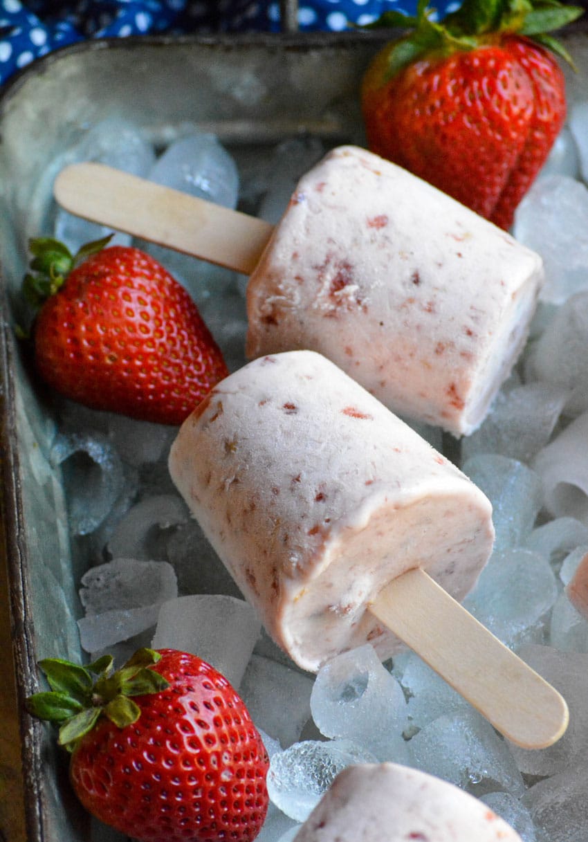 frozen strawberry cobbler pops on a bed of ice in a silver tray with fresh strawberries on the side