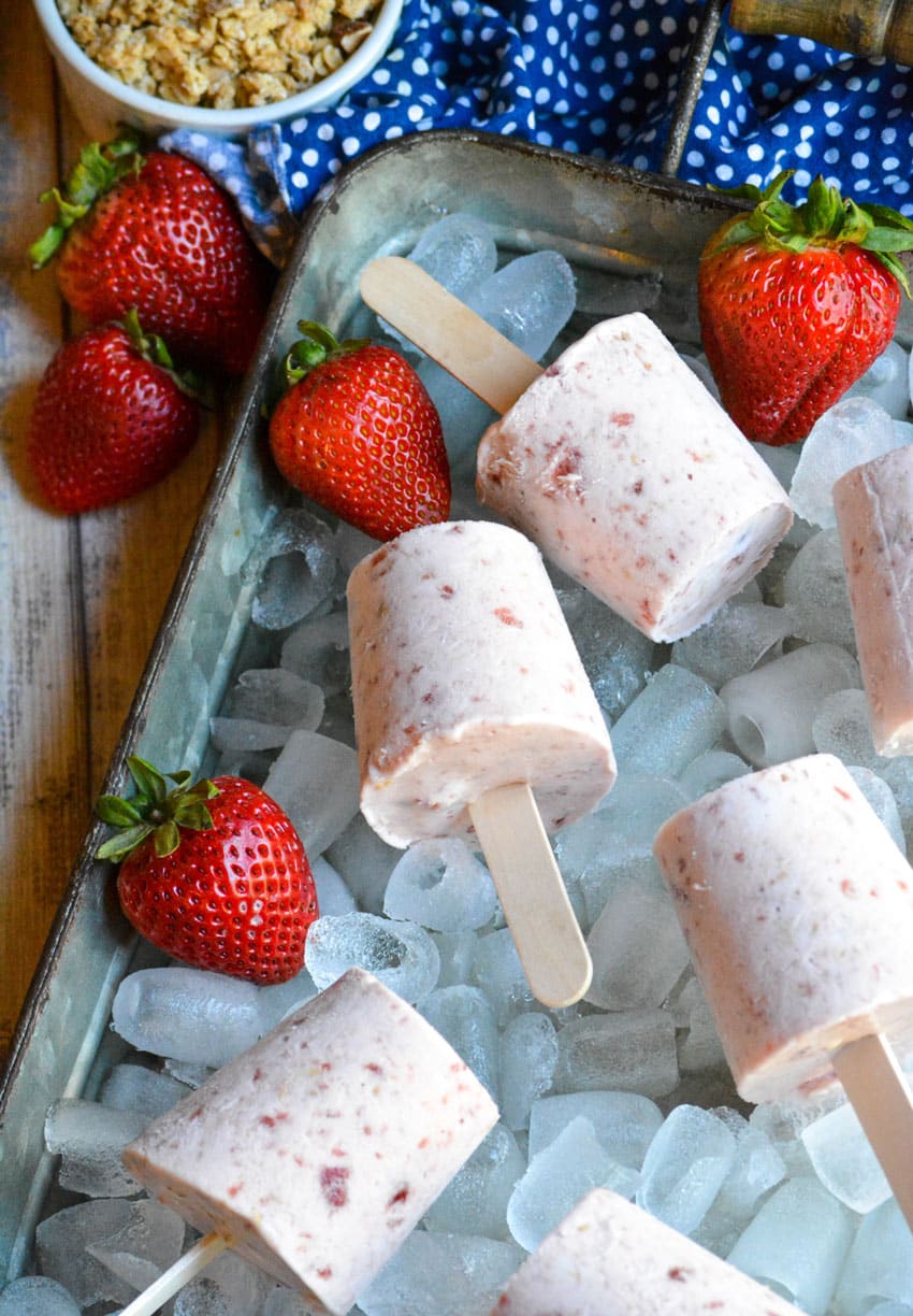 strawberry cobbler ice cream pops on wooden sticks laying on ice in a silver tray