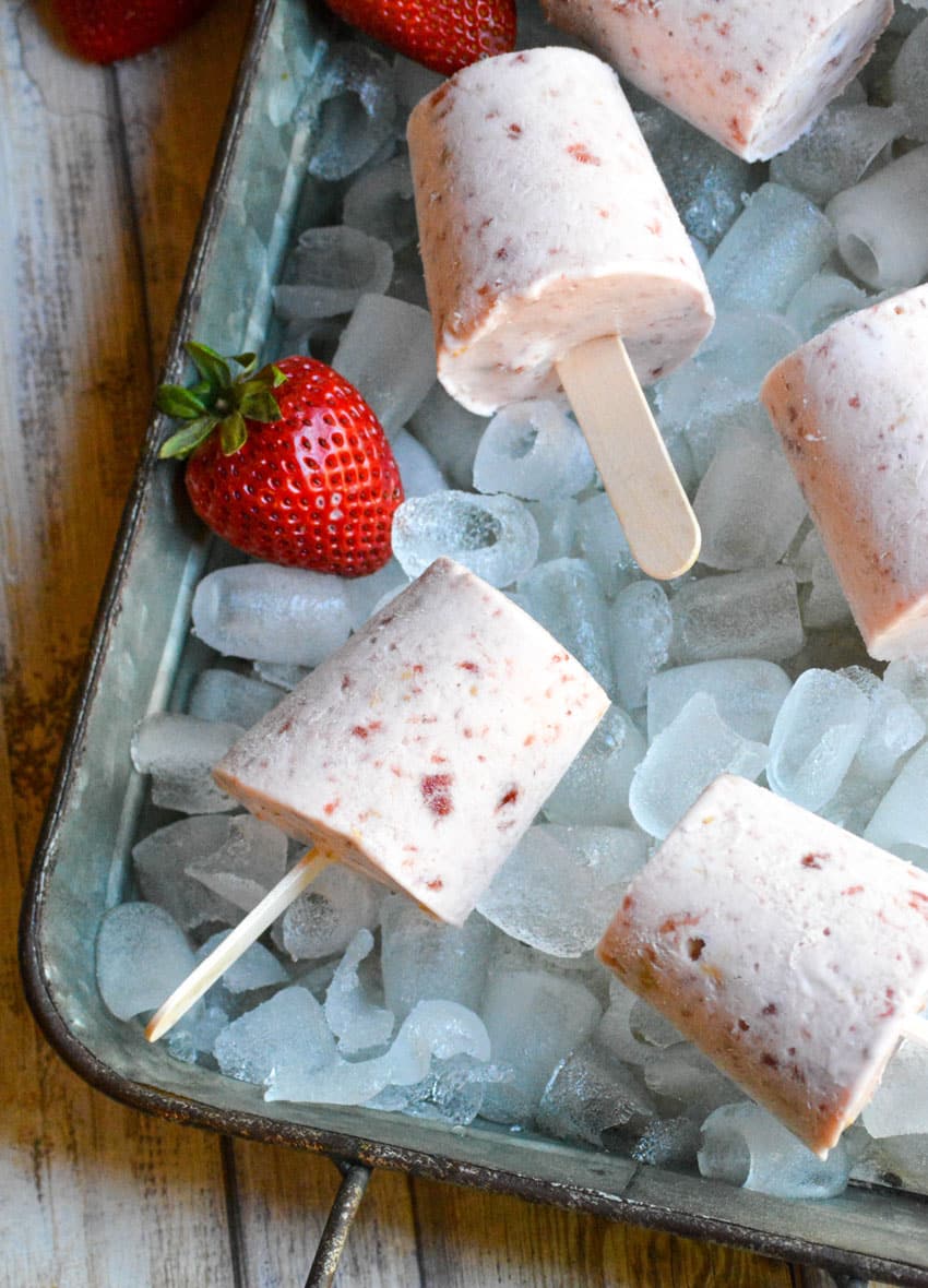 frozen strawberry cobbler pops on a bed of ice in a silver tray with fresh strawberries on the side