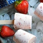 strawberry cobbler ice cream pops on wooden sticks laying on ice in a silver tray