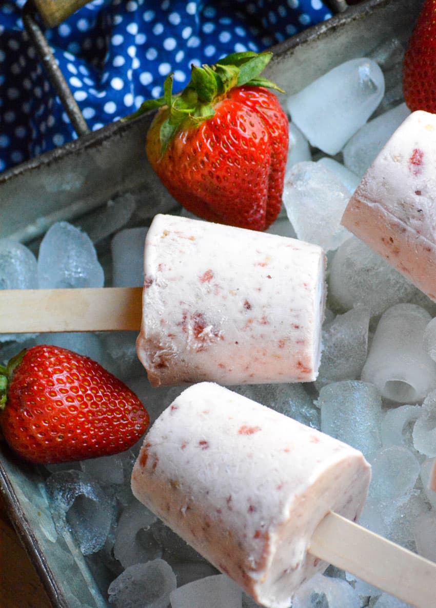 strawberry cobbler ice cream pops on wooden sticks laying on ice in a silver tray