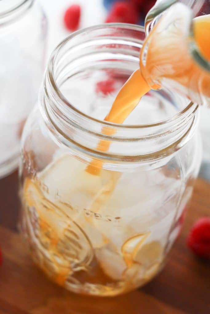 raspberry ice tea being poured over ice into a glass mason jar