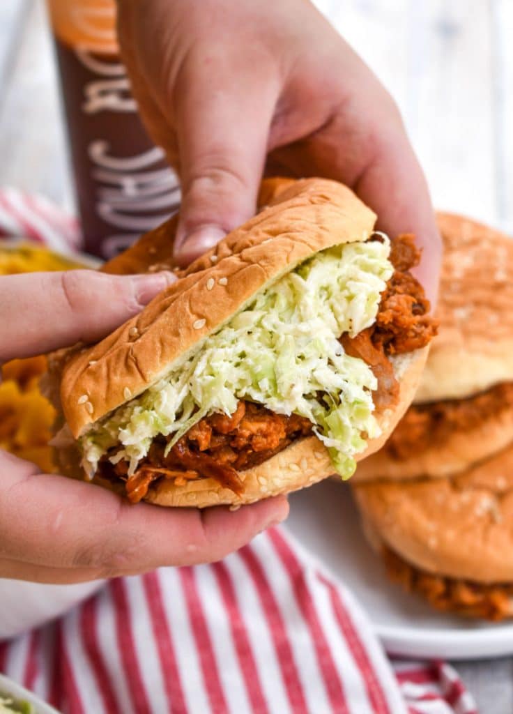 two hands holding up a barbecue sandwich topped with creamy two ingredient coleslaw recipe