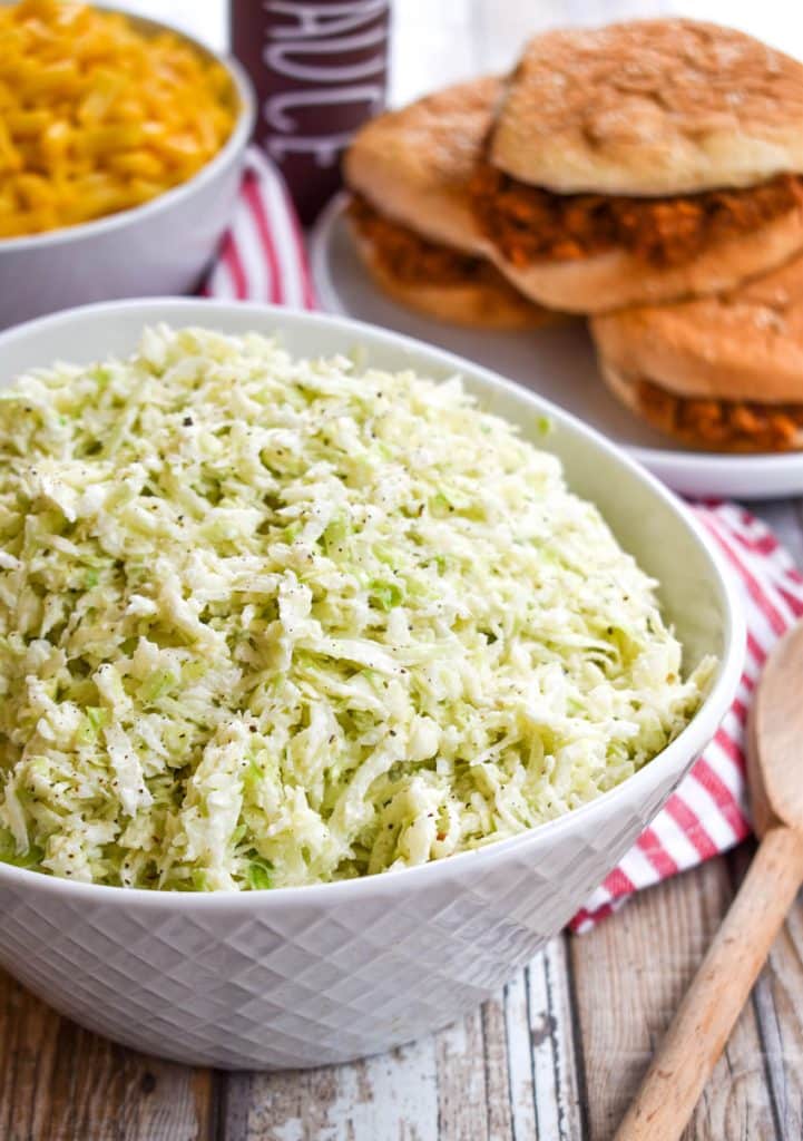 2 ingredient coleslaw in a white bowl in front of barbecue sandwiches