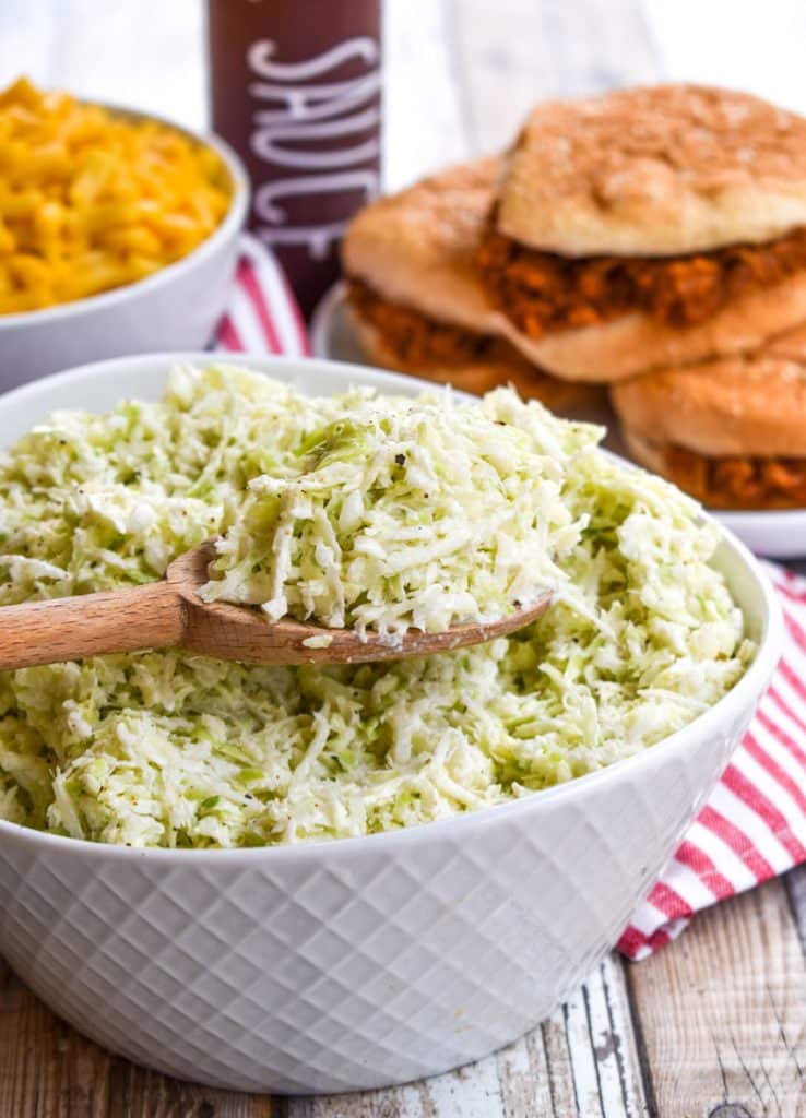 a wooden spoon holding a scoop of creamy coleslaw above a white bowl