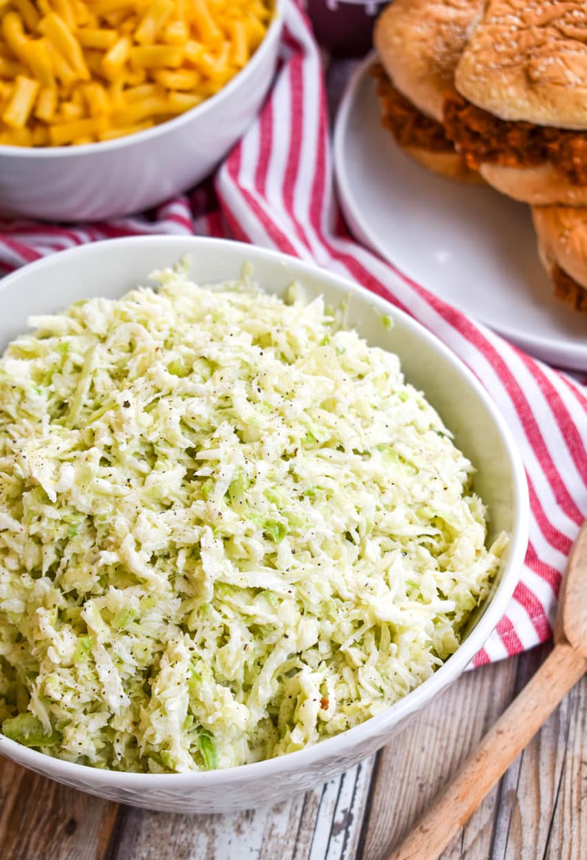 2 ingredient coleslaw in a white bowl in front of barbecue sandwiches