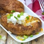 air fryer baked potatoes topped with sour cream, shredded cheese, and thinly sliced green onions