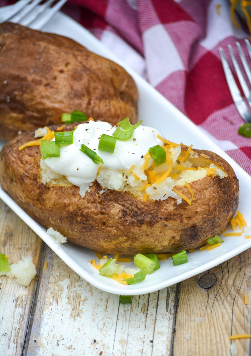 air fryer baked potatoes topped with sour cream, shredded cheese, and thinly sliced green onions
