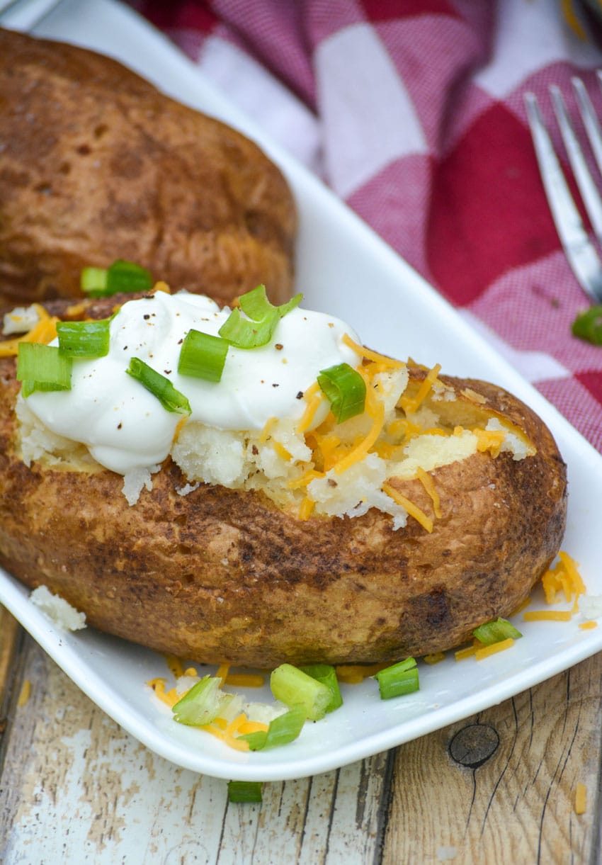 air fryer baked potatoes topped with sour cream, shredded cheese, and thinly sliced green onions